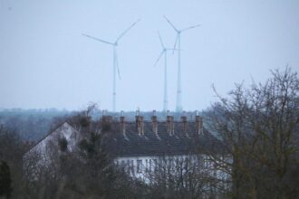 Ein Mehrfamilienhaus mit Windrädern im Hintergrund (Archiv)